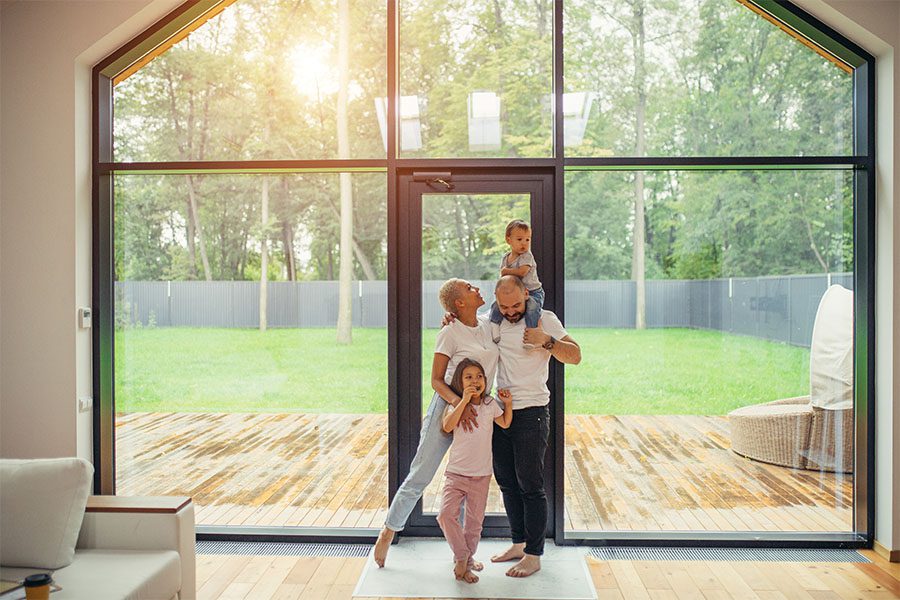 Blog - Portrait of a Family with Two Kids Standing in Their Living Room Next to a Full Length Glass Windows and Door with Views of the Patio and Green Backyard