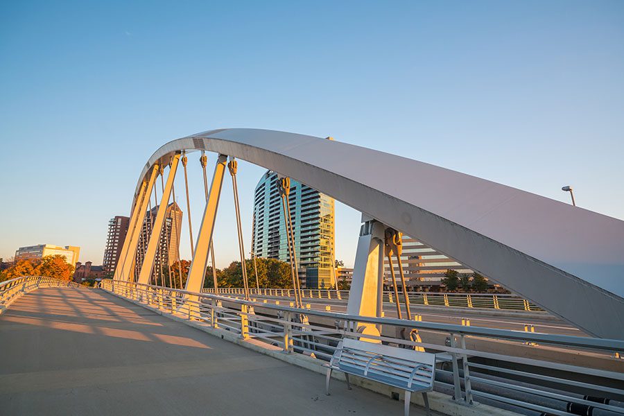 Contact - View of a Walking Bridge in Columbus Ohio with Views of Commercial Buildings in the Background During Sunset