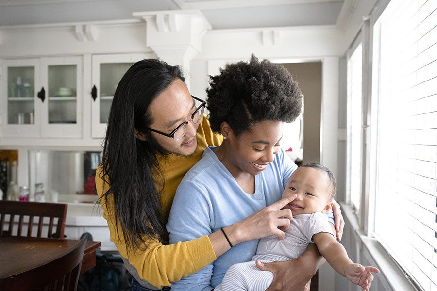 Personal Insurance - Closeup Portrait of Two Joyful Young Parents Standing in the Kitchen While Playing with Their Baby