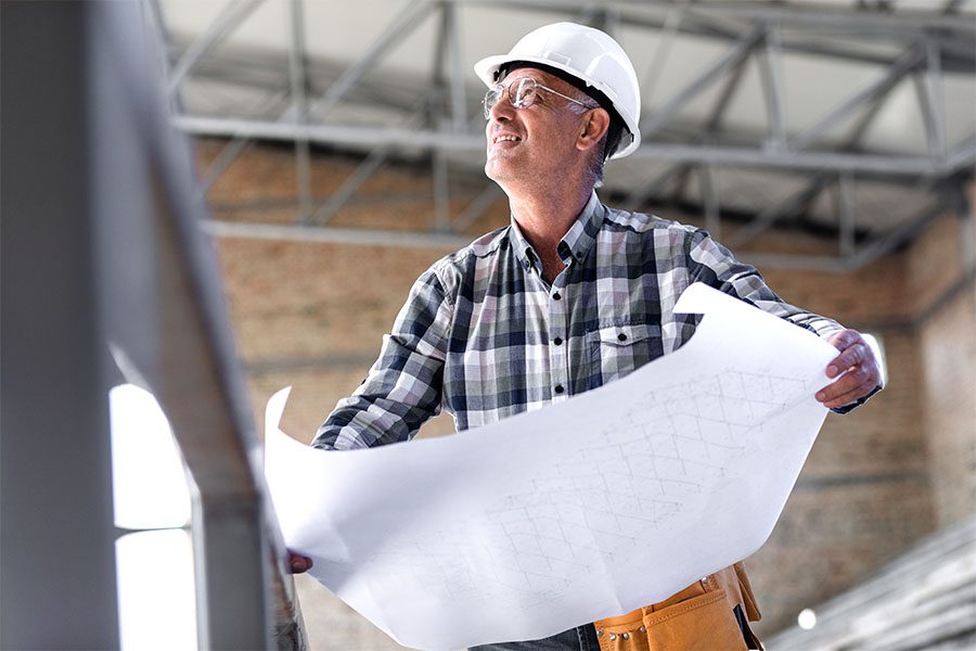 Specialized Business Insurance - Closeup Portrait of a Mature Contractor Holding Up New Building Blueprints While Standing on a Commercial Construction Jobsite