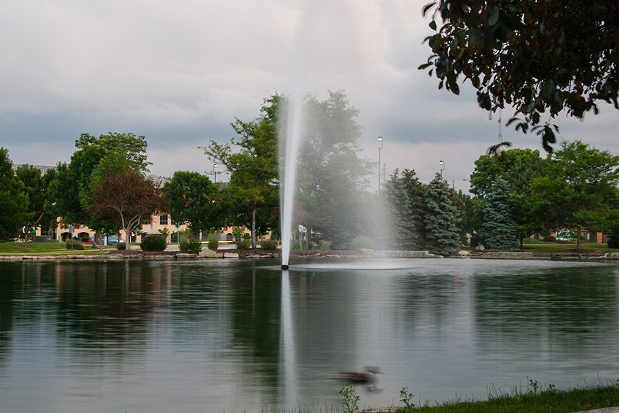Dublin, OH - Water Fountain in Lake With Trees Around it on a Semi Sunny Day