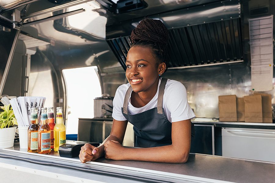 Food Truck Insurance - Smiling Woman in an Apron Leaning Over the Counter and Working in a Food Truck
